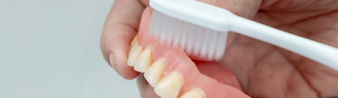 A patient brushing a their dentures to keep them clean